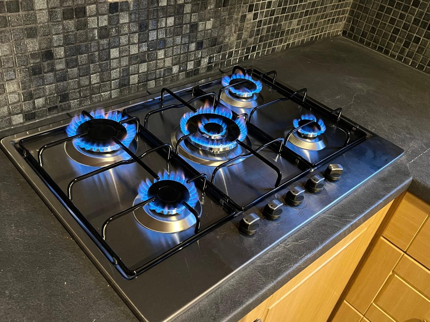 A five-burner gas hob lit blue, set into a worktop