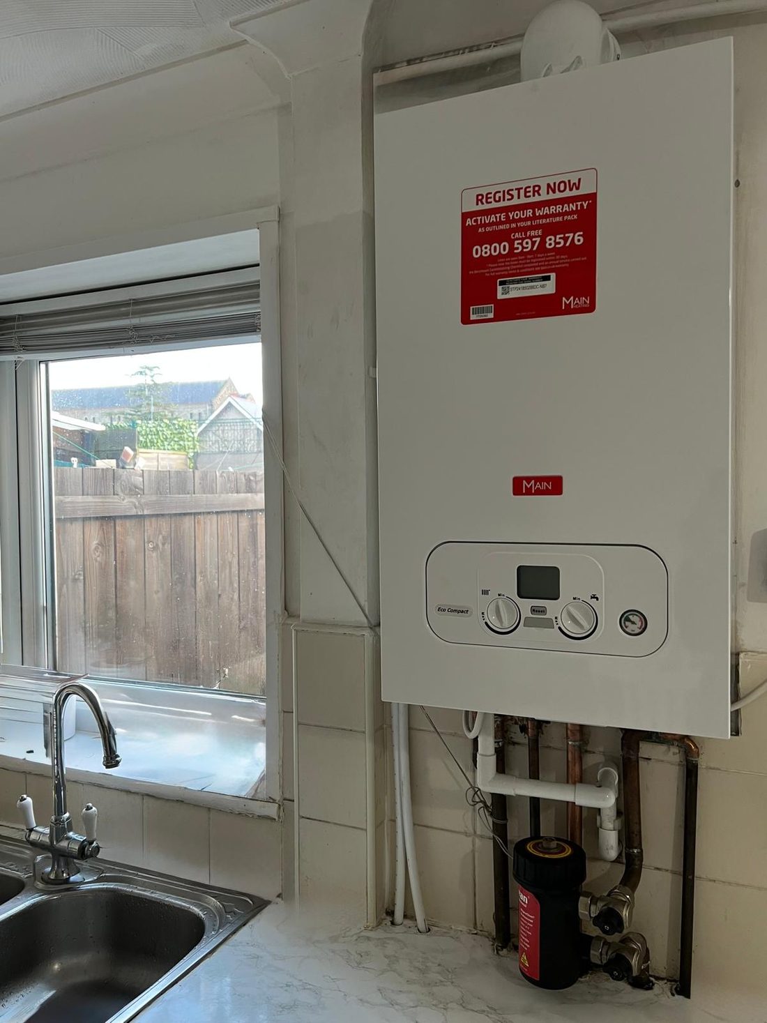 A combi boiler on a kitchen wall beside a window, with a sink below